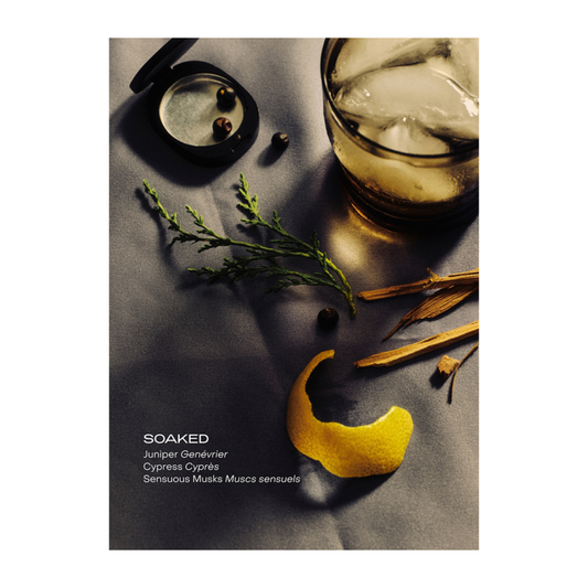 Scenic with a glass of whiskey, ice cubes, juniper berries, and a yellow crescent moon on a dark surface.