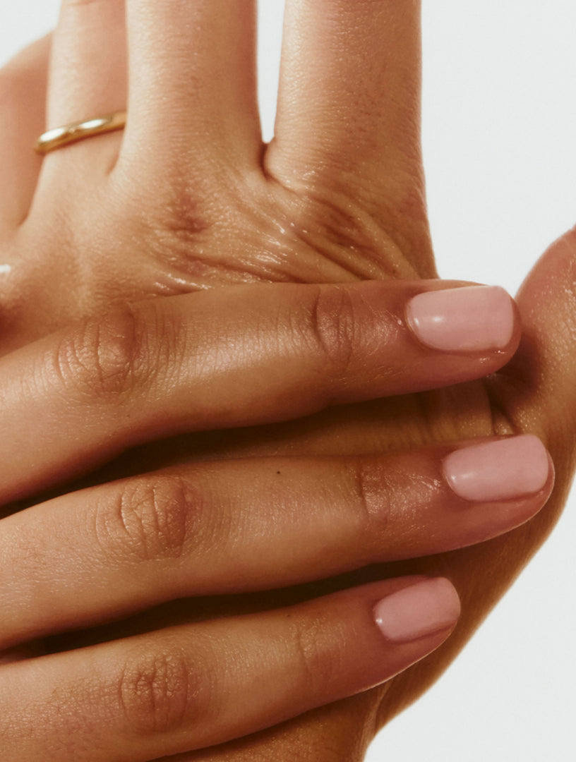 Close-up of a hand with pink nail polish on a neutral background